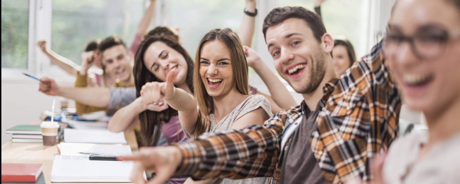 Cheerful students celebrating in classroom and looking at camera.