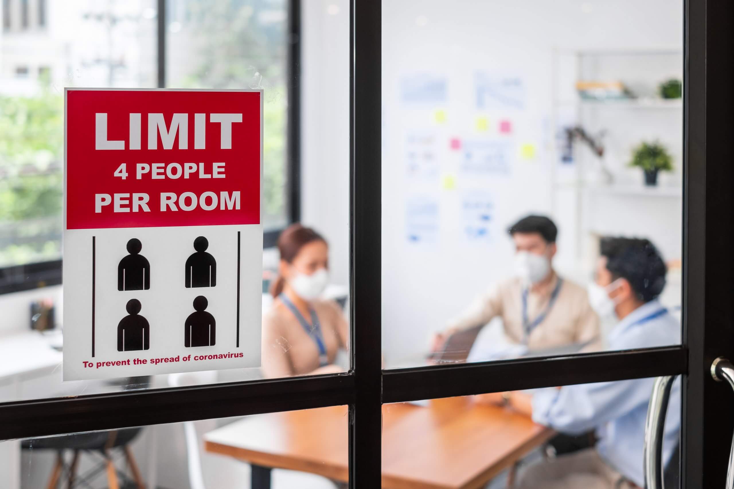 Limit people in meeting room sign over asian business people wear face mask working and meeting in office to protect infection of coronavirus covid-10 after lockdown, reopen new normal office concept Sign on meeting room displaying room capacity limit